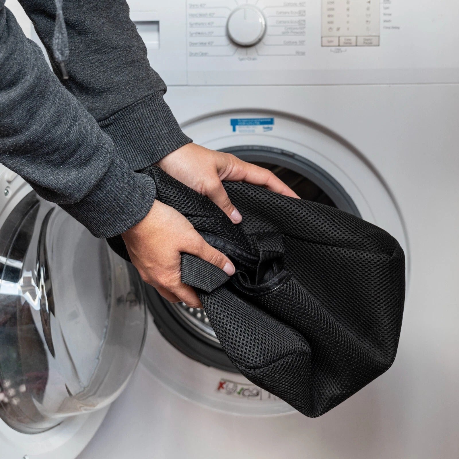Person holding a black mesh laundry bag in front of a washing machine.