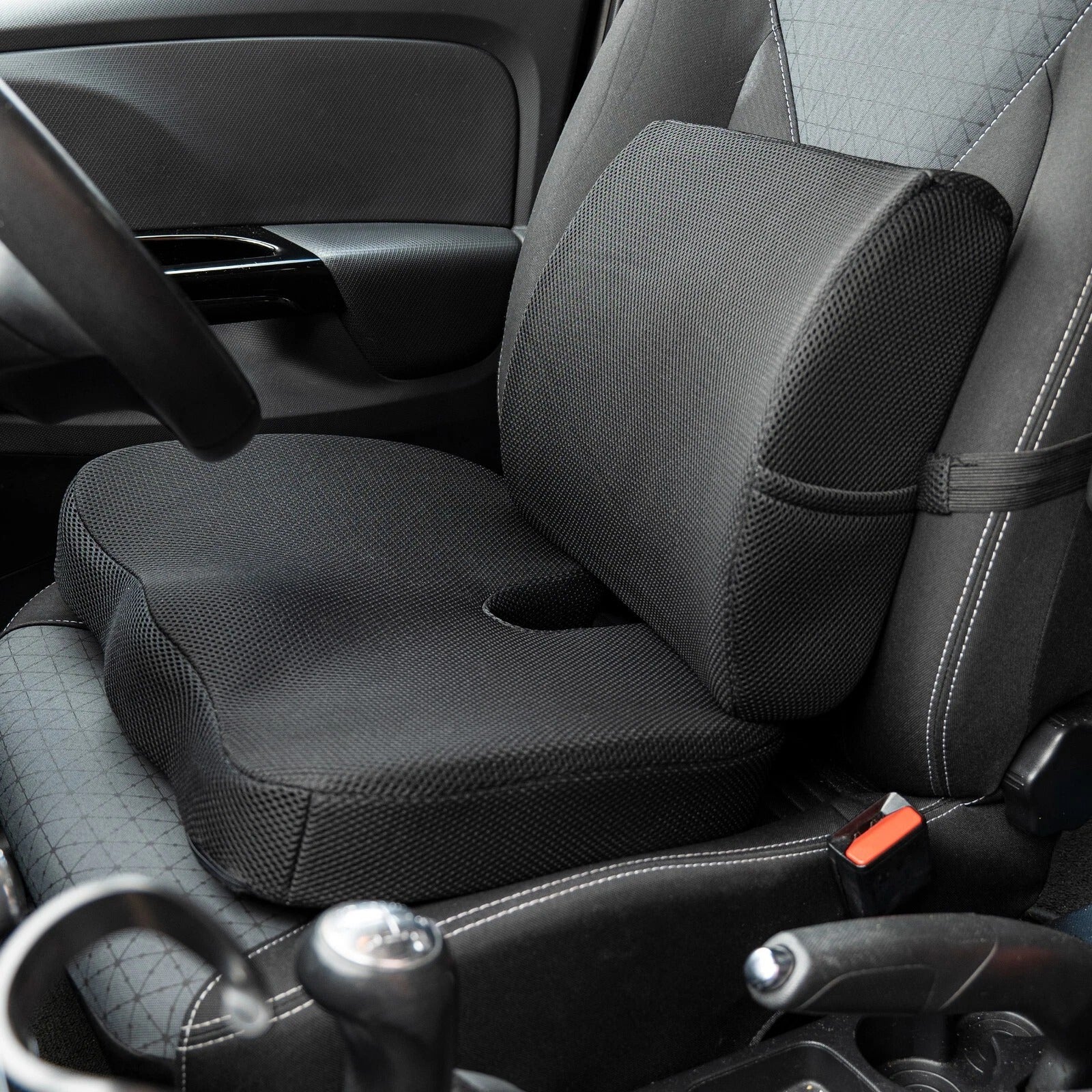 Car seat with a black ergonomic cushion on a gray car interior.