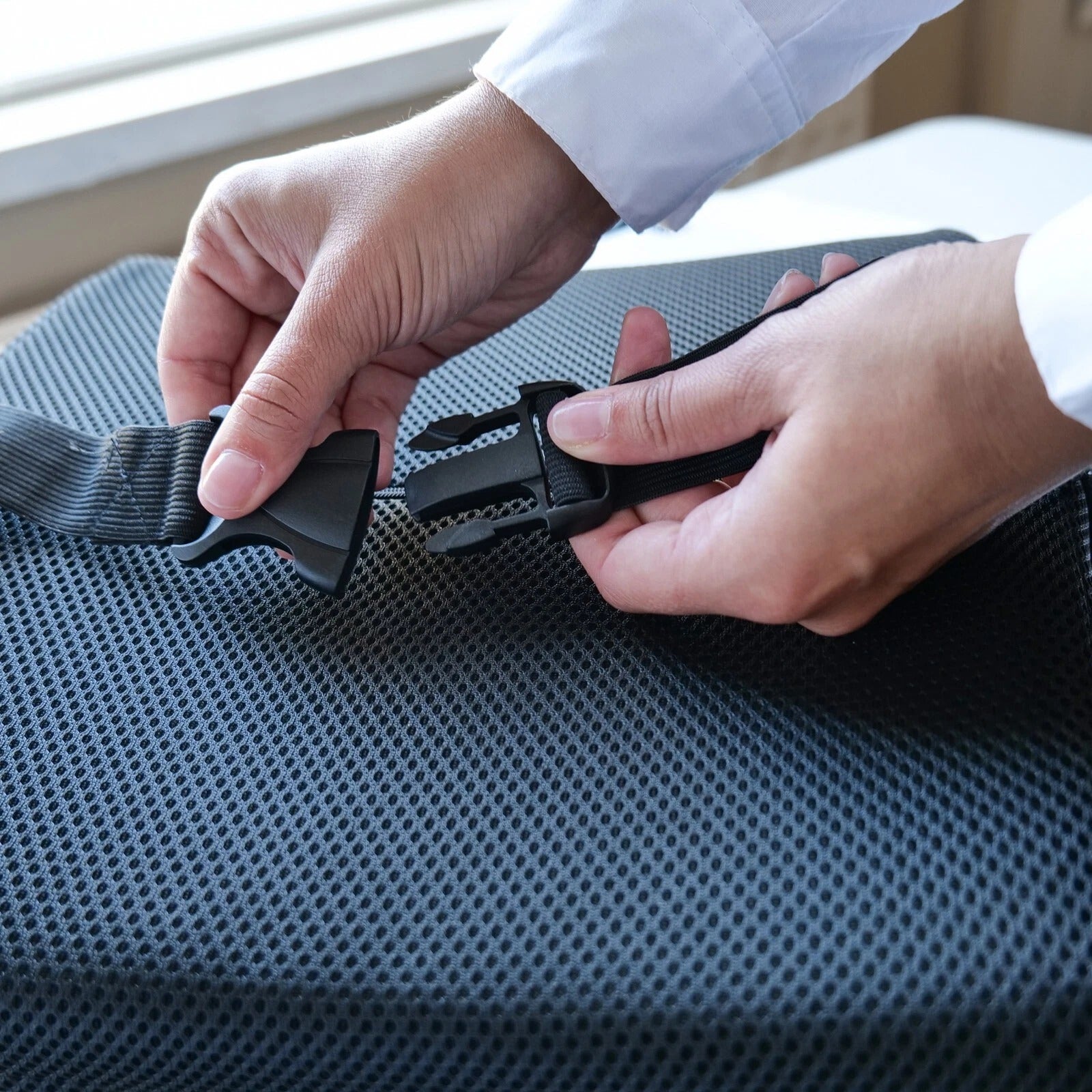 Person adjusting a black seat belt on a blue car seat.