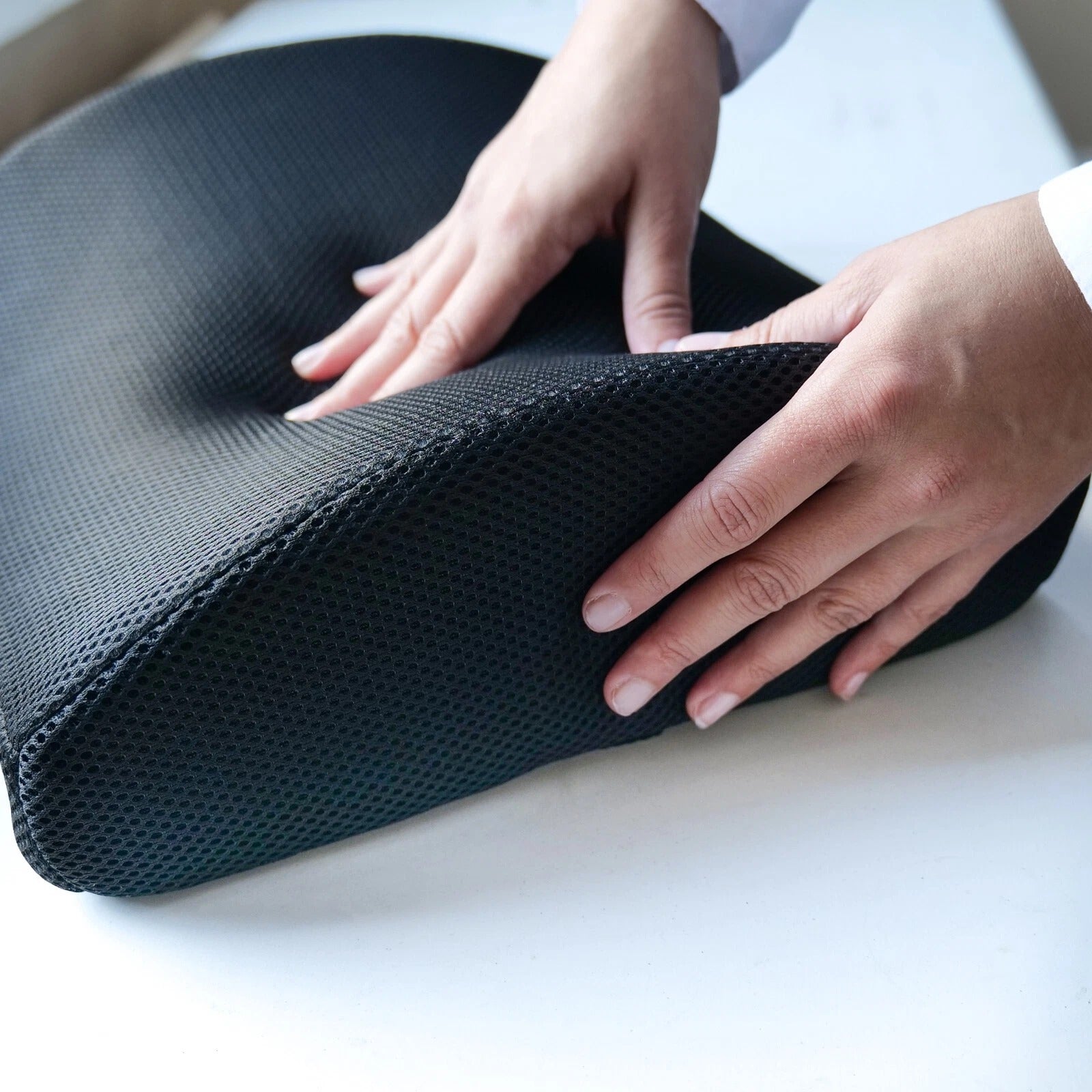 Person holding a dark gray memory foam cushion on a light surface